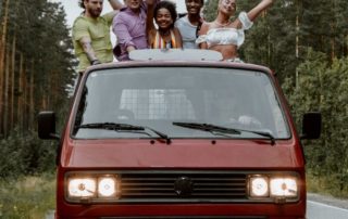 young people standing up riding in a red pickup truck