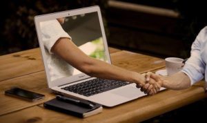 arm reaching out of laptop monitor to shake hand of person at desk